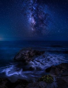 the night sky is filled with stars above the ocean and rocks in the foreground