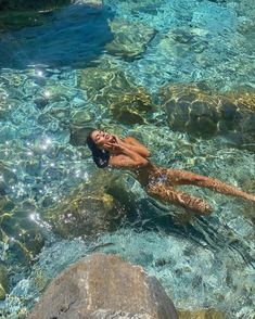 a woman is swimming in the clear blue water with rocks and boulders on either side