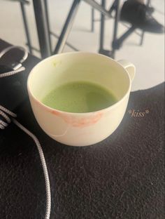 a white bowl filled with green liquid sitting on top of a black table next to an electric cord