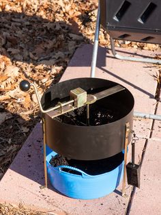 a blue barrel sitting on top of a sidewalk next to a trash can with a metal handle