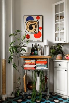 a kitchen with a potted plant on top of a metal cart in front of a painting