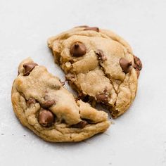 two chocolate chip cookies sitting on top of a white counter next to one cookie broken in half