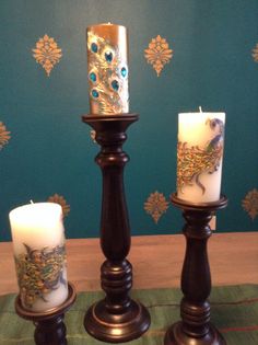 three candles sitting on top of a wooden table next to a wallpapered wall