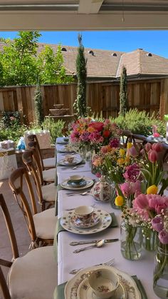 a long table with plates and flowers in vases on top of it next to a wooden fence