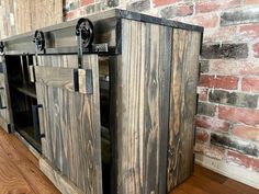 an entertainment center made out of wood with metal hardware on the doors and drawers, in front of a brick wall