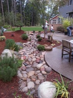 a garden with rocks and plants in the foreground, two people sitting at a table