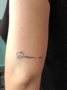 a woman with a tattoo on her arm that says dream in cursive writing