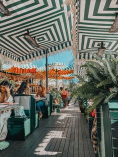 people are sitting under umbrellas at an outdoor cafe on a deck with tables and chairs