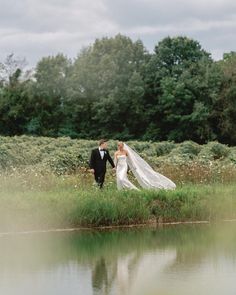 a bride and groom are walking by the water