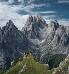 the mountains are covered in snow and green grass, under a blue sky with clouds