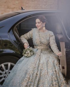 a woman standing next to a car wearing a blue dress and holding a bouquet in her hand