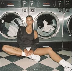 a woman sitting on the floor in front of a washer and dryer with her legs crossed