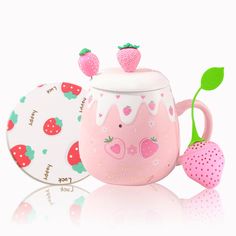 a pink cup with strawberries on it next to a plate and strawberry shaped coaster