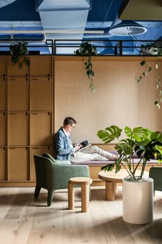 a man sitting on a chair in front of a plant and looking at a book