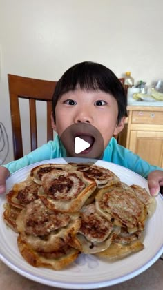 a little boy sitting in front of a plate of food