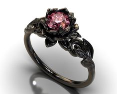 "If you're looking for an engagement ring like no other, stop right here. This AMAZING piece of fine jewelry is the perfect expression of your eternal love. Its BLACK colors bring out the beauty of this ring. This engagement ring is created of gleaming, 14kt black gold, carved into an elaborate leaf design at the top. A striking Pink Sapphire sits boldly at the center, surrounded by black gold petals, forming the eye-catching image of a lotus flower. Item Specifics: (1 Ring Only) Gem Details: Ce Pink And Black Engagement Ring, Black And Pink Wedding Rings, Elegant Black Flower Promise Ring, Black Flower Ring For Wedding, Elegant Black Flower Ring For Anniversary, Elegant Black Flower Ring For Wedding, Elegant Black Flower Ring, Grunge Engagement Ring, Rose Engagement Rings