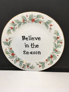 a white plate with the words believe in the season on it and holly leaves around it