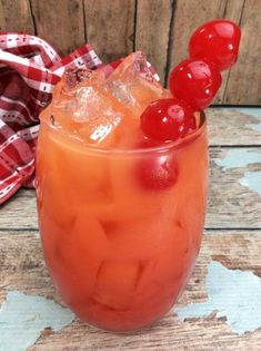 a drink with ice and cherries on the rim sitting on a wooden table next to a plaid napkin