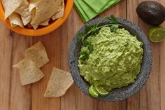 a bowl filled with guacamole next to some chips and lime wedges