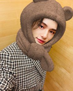 a young man wearing a bear hat and scarf over his head, standing in front of a wooden wall