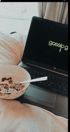 an open laptop computer sitting on top of a bed next to a bowl of cereal