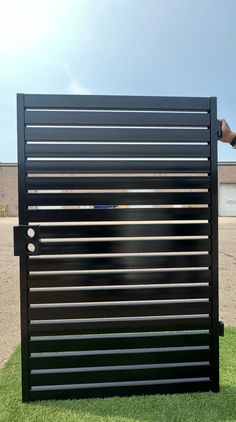 a person is holding their hand up to a black gate that has vertical slats on it