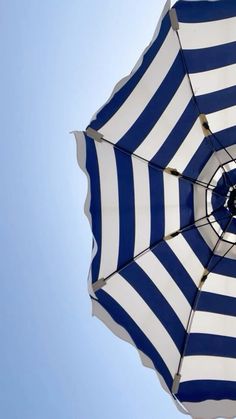 an open umbrella with blue and white stripes on the outside, against a clear blue sky