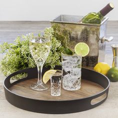 a tray with glasses and bottles on it next to lemons, limes and an ice bucket