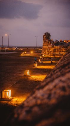 people are sitting on benches near the water at night with candles lit up in front of them