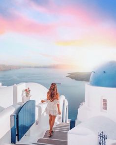 a woman standing on top of a white building next to the ocean with stairs leading up to it