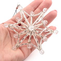 a hand holding a small silver and clear snowflake ornament