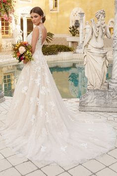 a woman standing in front of a fountain wearing a wedding dress with an open back