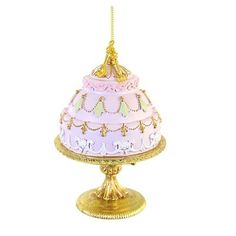 a pink and white cake on a gold plate with a chain hanging from the top