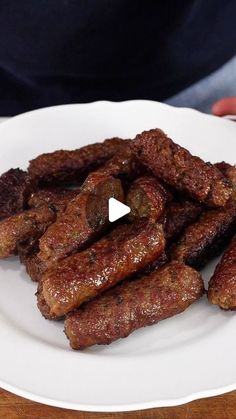 a white plate topped with sausages on top of a wooden table next to a person