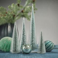 three glass christmas trees sitting on top of a table next to balls and vases