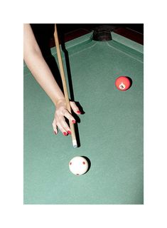 a woman's hand reaching for a pool ball with two cues in front of her