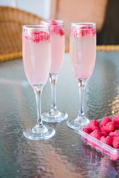 three wine glasses with raspberries in them sitting on a table next to some strawberries