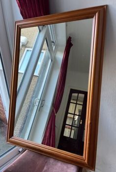 a mirror hanging on the side of a wall next to a purple chair and window