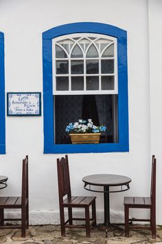 three chairs and a table in front of a white building with blue trim around the windows