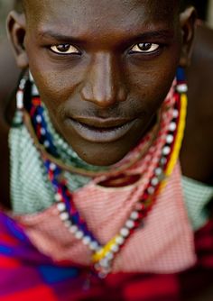 an african man with multiple necklaces on his neck and chest, looking at the camera