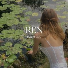 a woman in white dress sitting next to lily pads and looking at water lilies