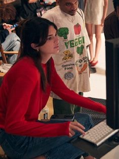 a woman sitting in front of a computer monitor next to a man standing behind her