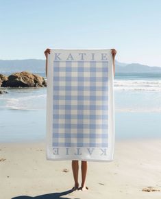 a person holding up a blue and white towel on the beach with water in the background