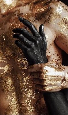 a man covered in gold and black paint with his hands on his chest, wearing gloves