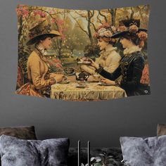 two women sitting at a table in front of a wall tapestry