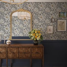 a table with flowers on it in front of a mirror and wallpapered walls