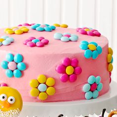 a pink cake decorated with flowers and a yellow chick on the side, sitting on a white pedestal