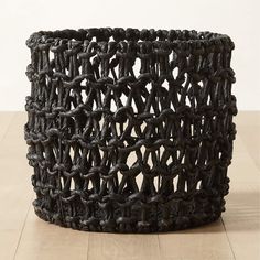 a large black basket sitting on top of a wooden floor next to a white wall