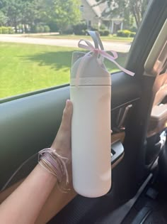 a person holding onto a white water bottle in the passenger seat of a car with a pink ribbon on it