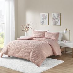 a bed with pink comforter and pillows in a room next to a window,